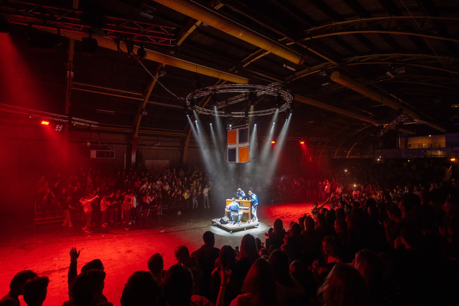 De lustrumreceptie met publiek rondom een verlicht podium en het P.E.B.-wapen